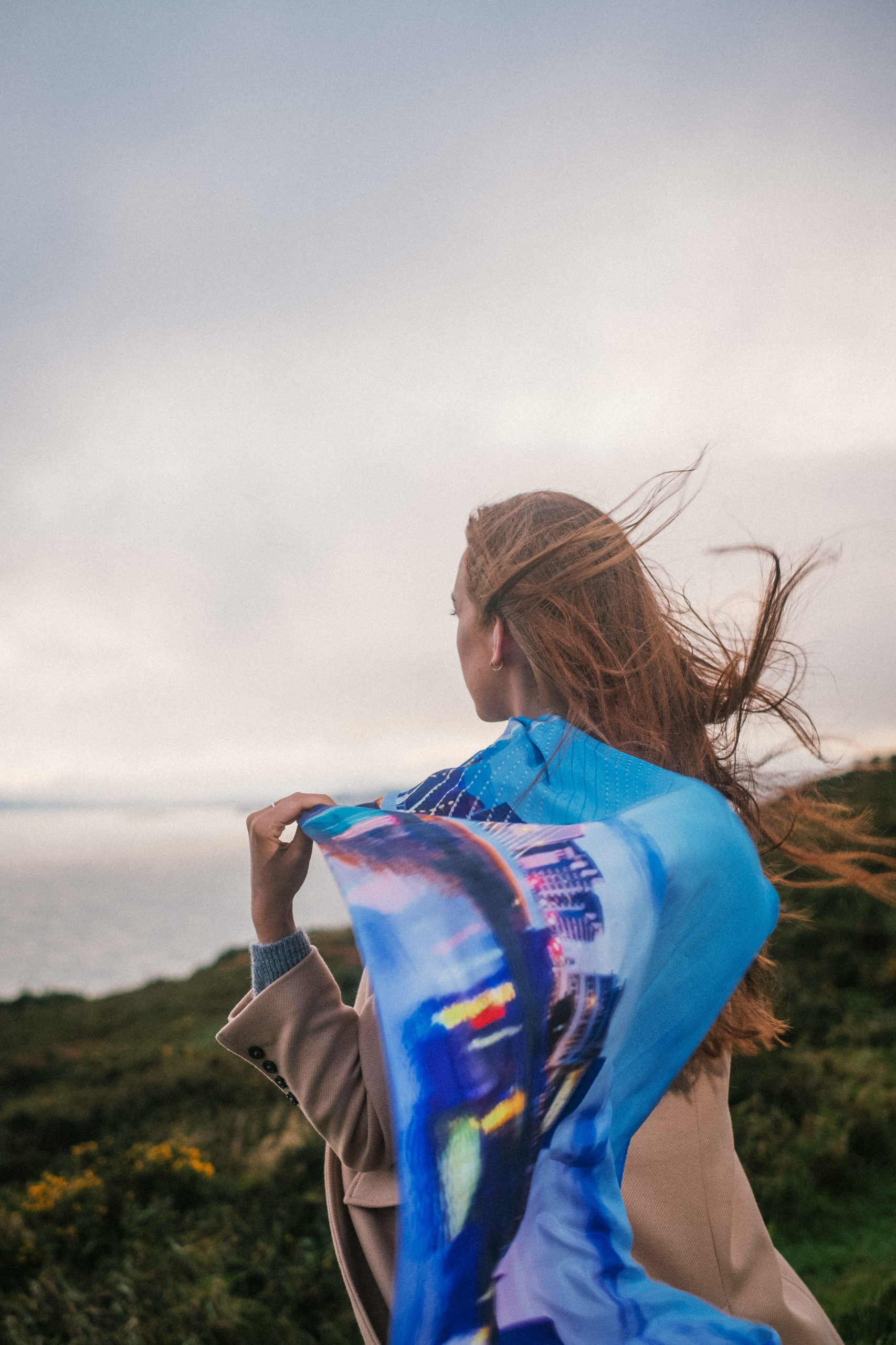 Young woman, red hair blowing in the wind. standing near a cliff with a silk scarf