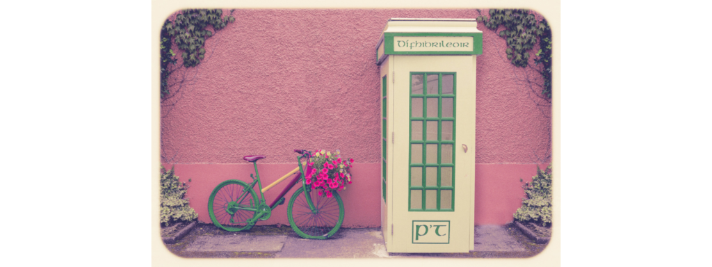 An old Irish telephone box set next to a pink wall and a colourful bike.